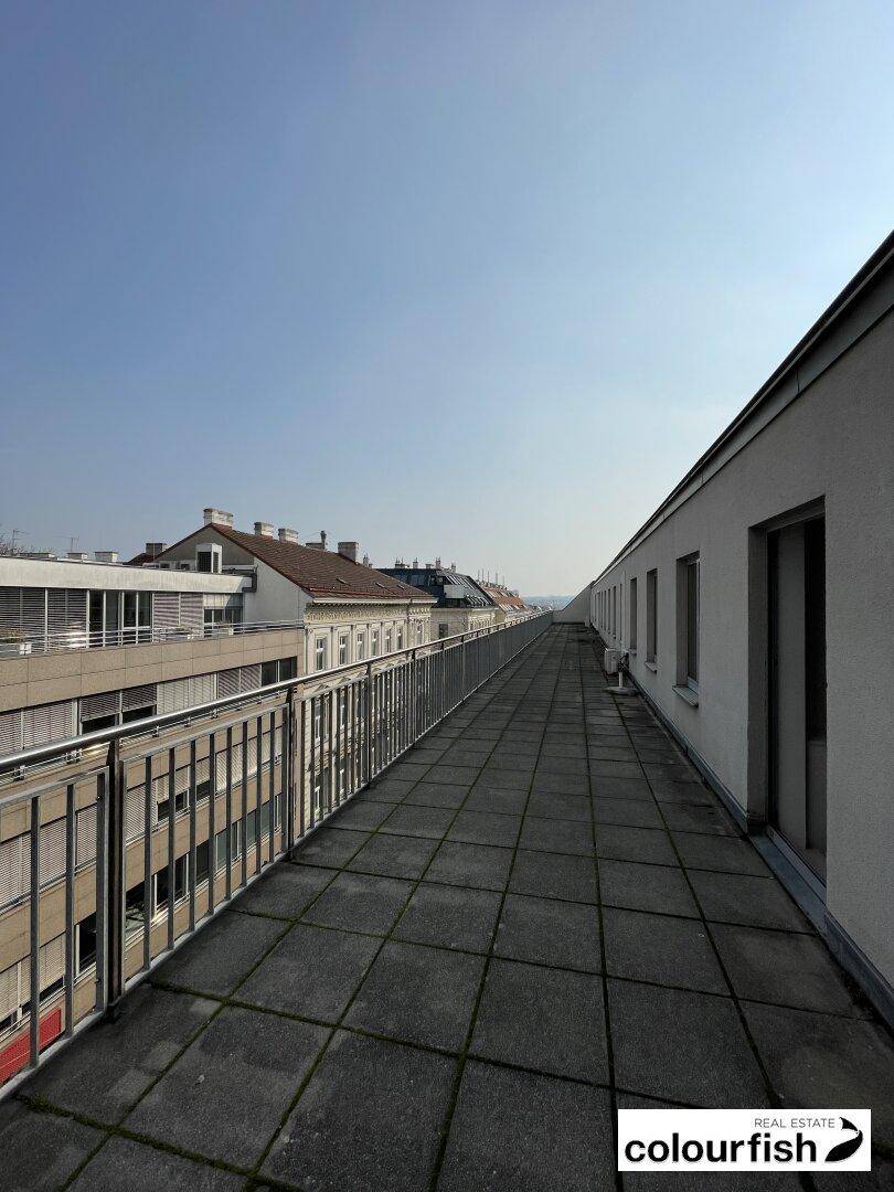 Lange, schmale Dachterrasse mit Fliesenboden und Metallgeländer, bietet einen weiten Blick über die Dächer der Stadt.