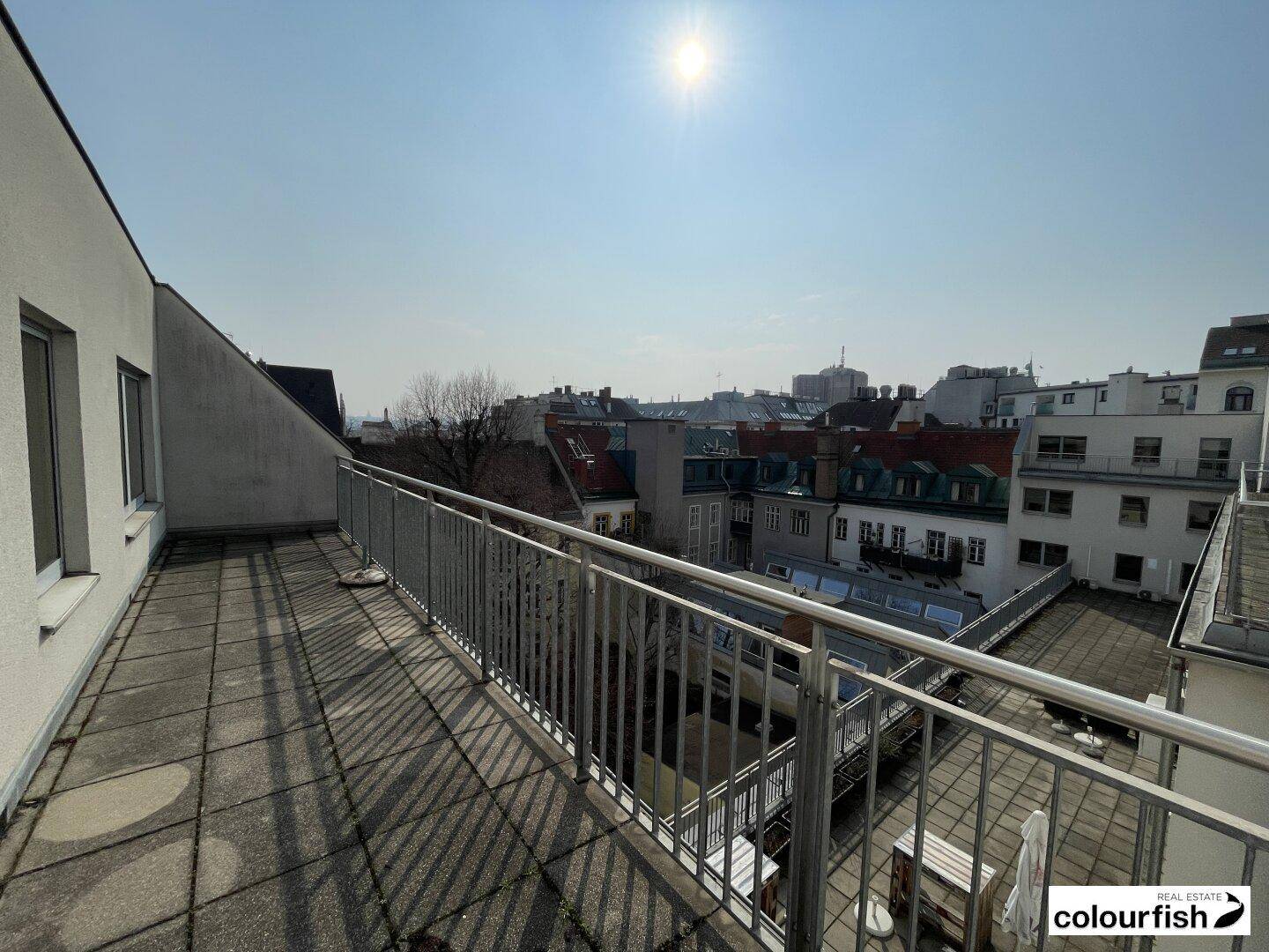 Geräumige Dachterrasse mit Fliesenboden und Metallgeländer, bietet einen sonnigen Ausblick auf die umliegende Stadtlandschaft.