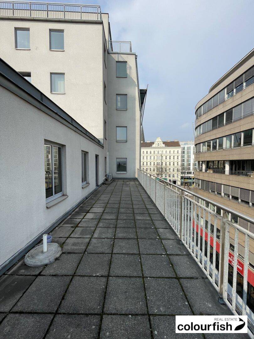 Geräumige Dachterrasse mit grauen Fliesen und Blick auf umliegende Gebäude und die Stadtlandschaft.