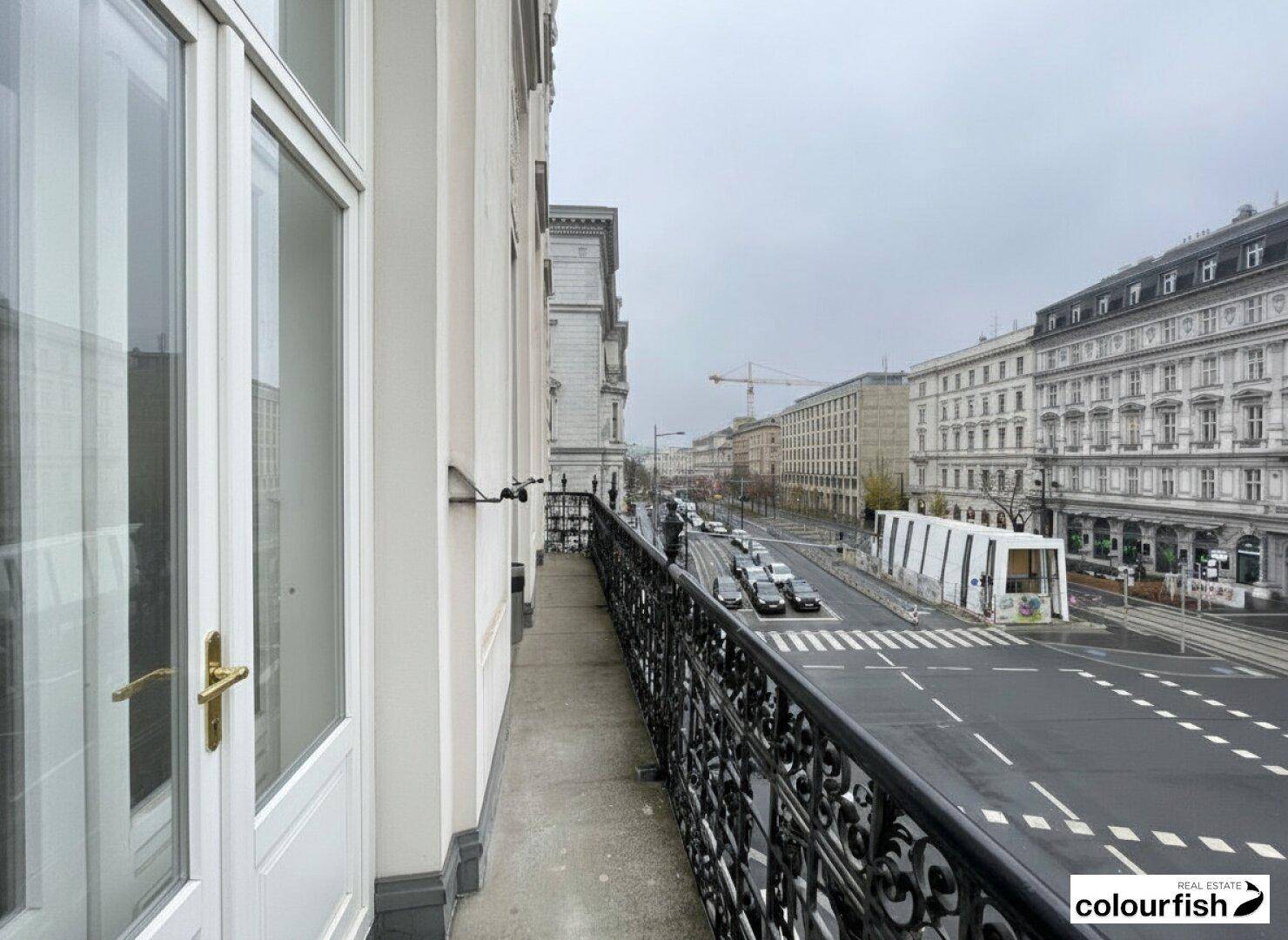 Langer Balkon mit schmiedeeisernem Geländer und Blick auf eine belebte Stadtstraße.