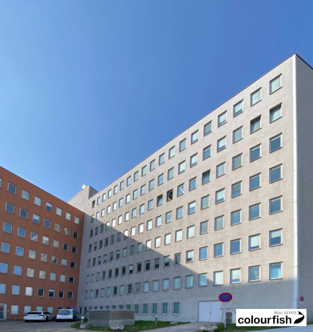 Modernes Bürogebäude mit zwei Flügeln und vielen Fenstern unter klarem blauem Himmel.