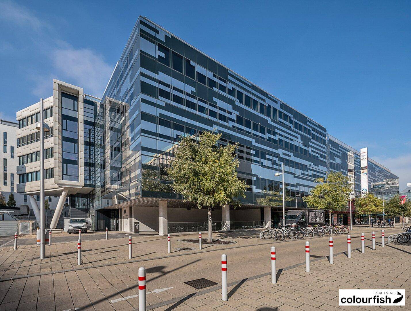 Modernes Bürogebäude mit auffälliger Glasfassade und geometrischen Mustern unter blauem Himmel.
