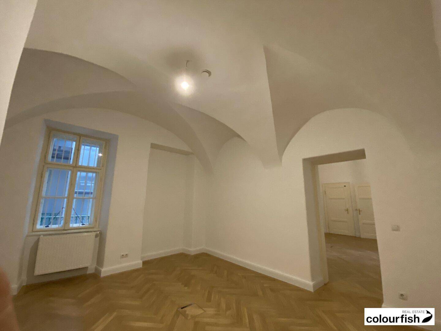 Einzigartiger Raum mit beeindruckender Gewölbedecke, Fischgrätparkett und einem Fenster, das Tageslicht hereinlässt.
