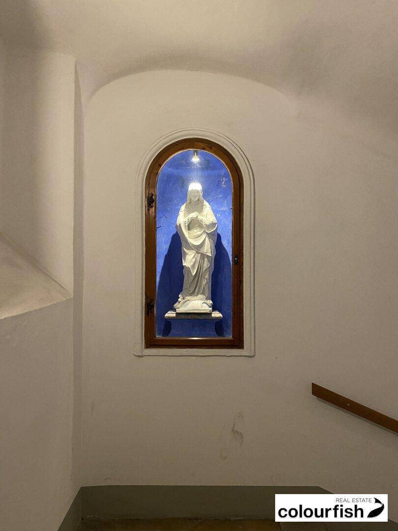 Treppenhaus mit einer beleuchteten Nische, die eine religiöse Statue beherbergt, in einem historischen Gebäude.
