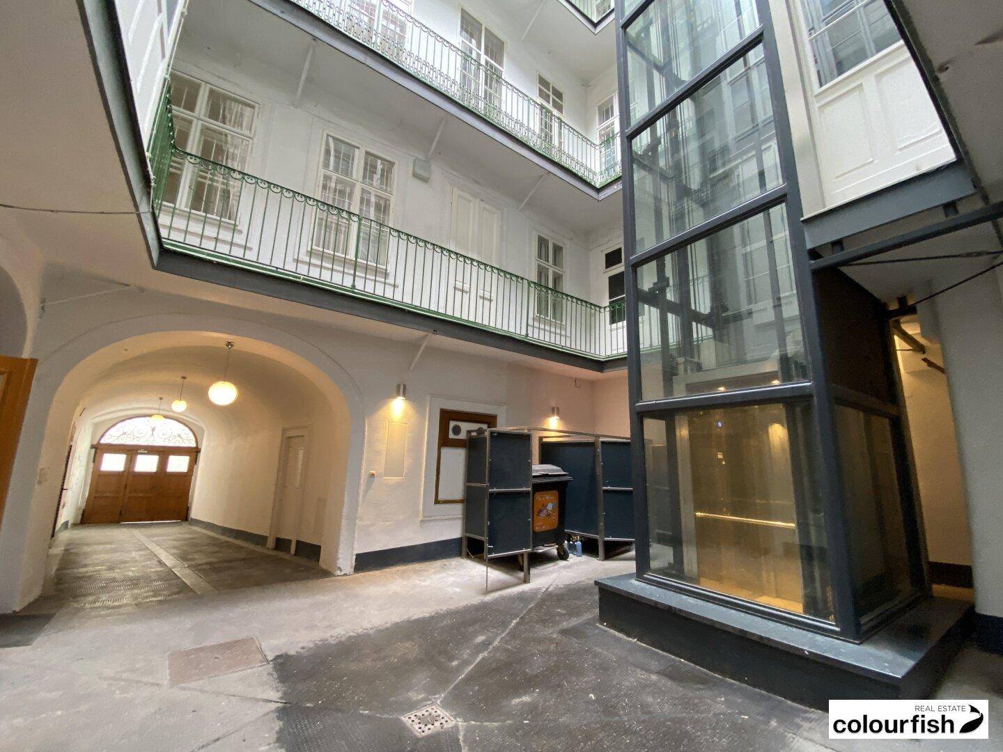 Innenhof eines Altbaus mit modernem Glasaufzug und Zugang zu den oberen Etagen.