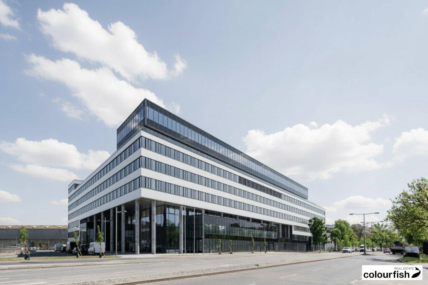 Modernes Bürogebäude mit markanter weißer Fassade und großen Glasfenstern, gelegen an einer belebten Straße unter blauem Himmel.