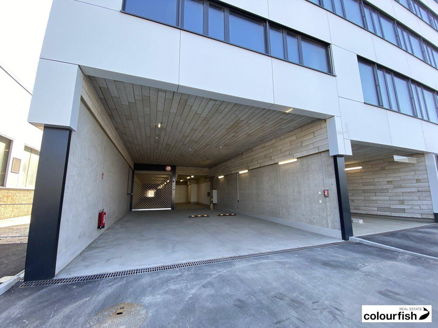 Einfahrt zur Tiefgarage eines modernen Gebäudes mit Betonwänden und Rolltor.