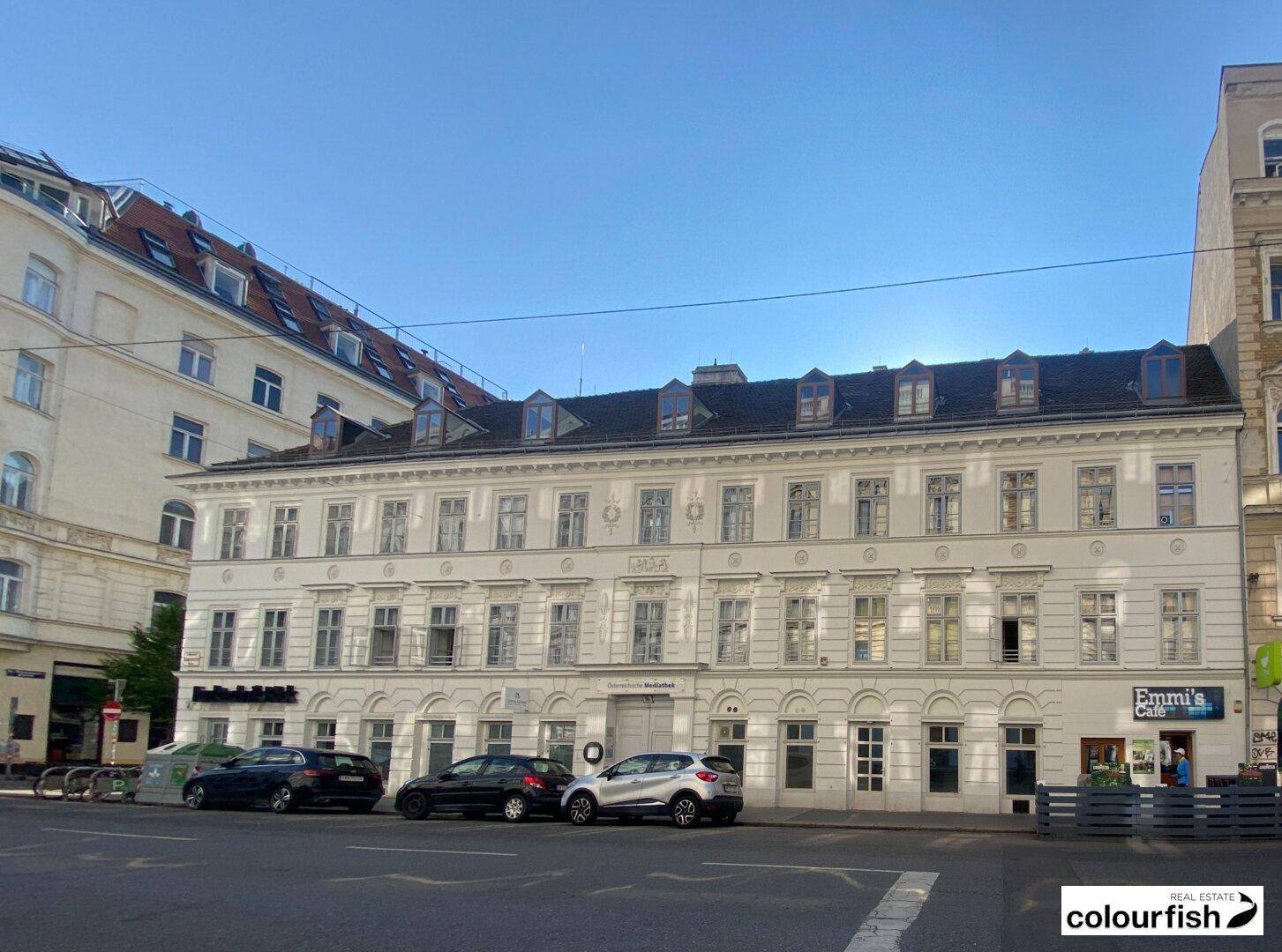 Breitere Ansicht der historischen Fassade mit vielen Fenstern und Geschäften im Erdgeschoss.