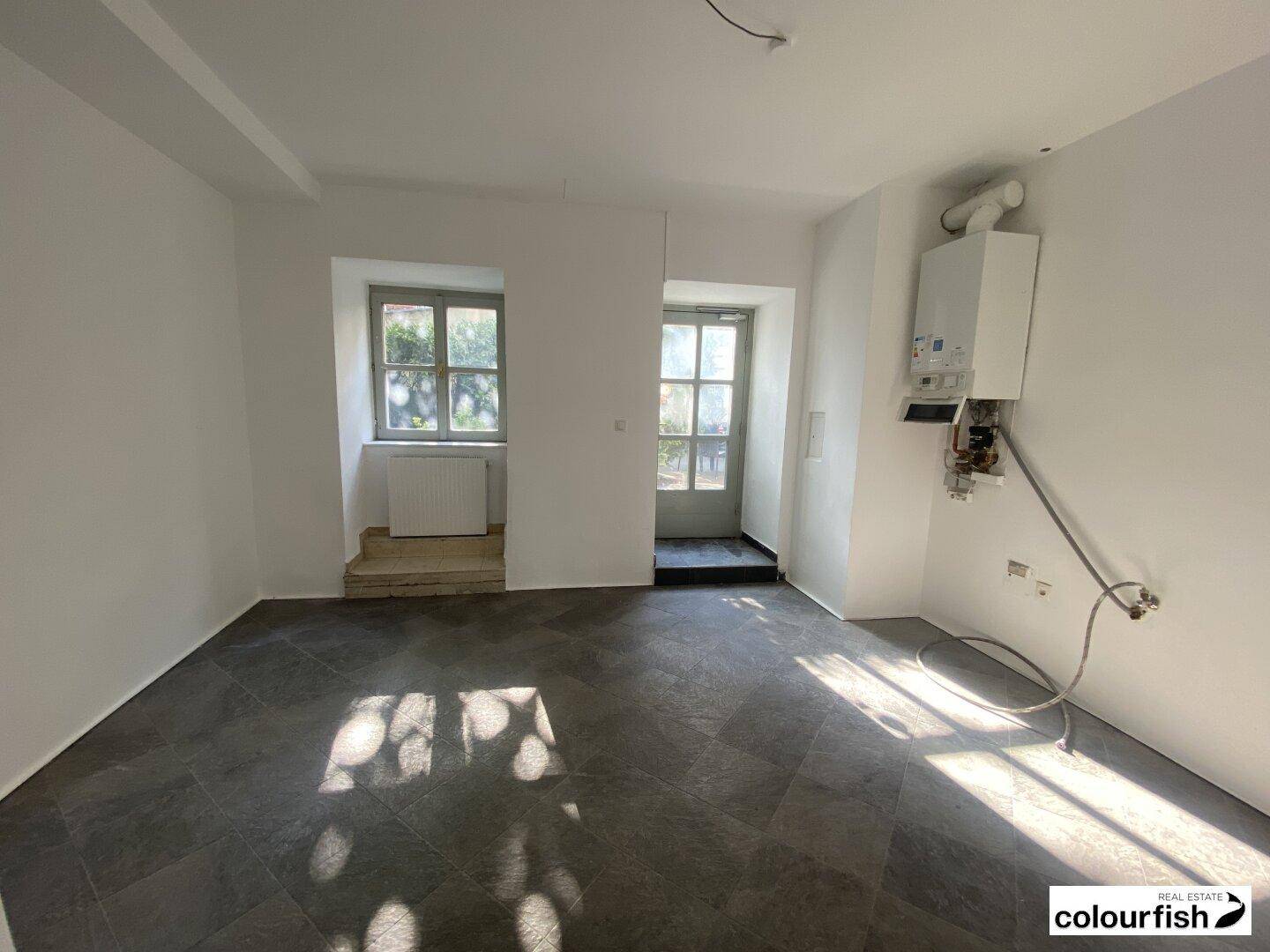 Teil des Gewerberaums mit Gastherme an der Wand, Fliesenboden und Fenster zum Innenhof.