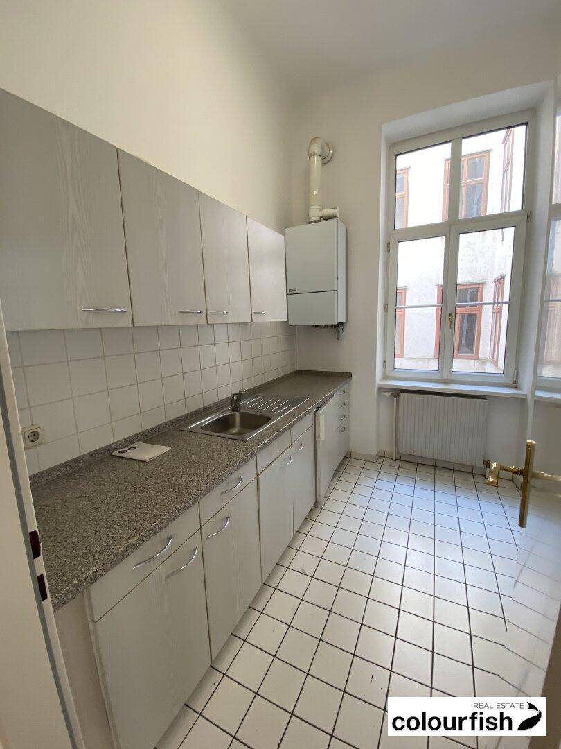 Funktionale Küche mit weißen Fliesen, Einbauschränken und einem Fenster für natürliche Belüftung.