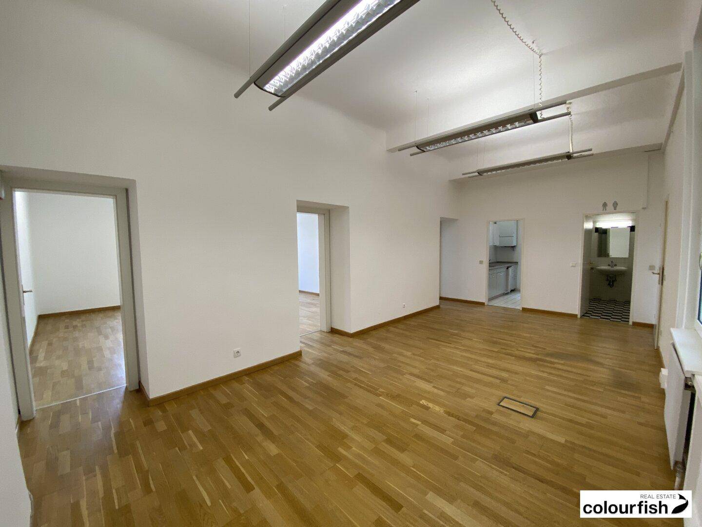 Offener Bürobereich mit Holzboden und Zugang zu weiteren Räumen, ideal für flexible Nutzung.