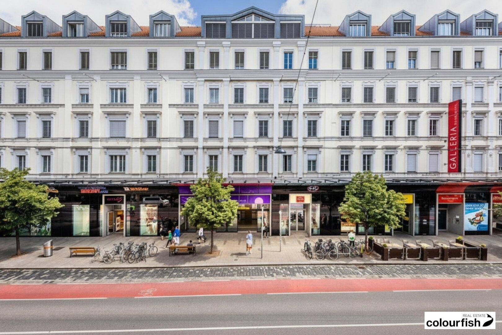 Klassisches Mehrfamilienhaus mit eleganter Fassade, Geschäften im Erdgeschoss und Wohnungen darüber, an einer belebten Straße gelegen.