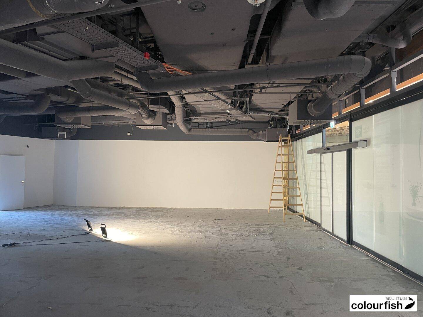 Geräumiger Gewerberaum mit freiliegenden Deckeninstallationen und großen Fensterfronten.
