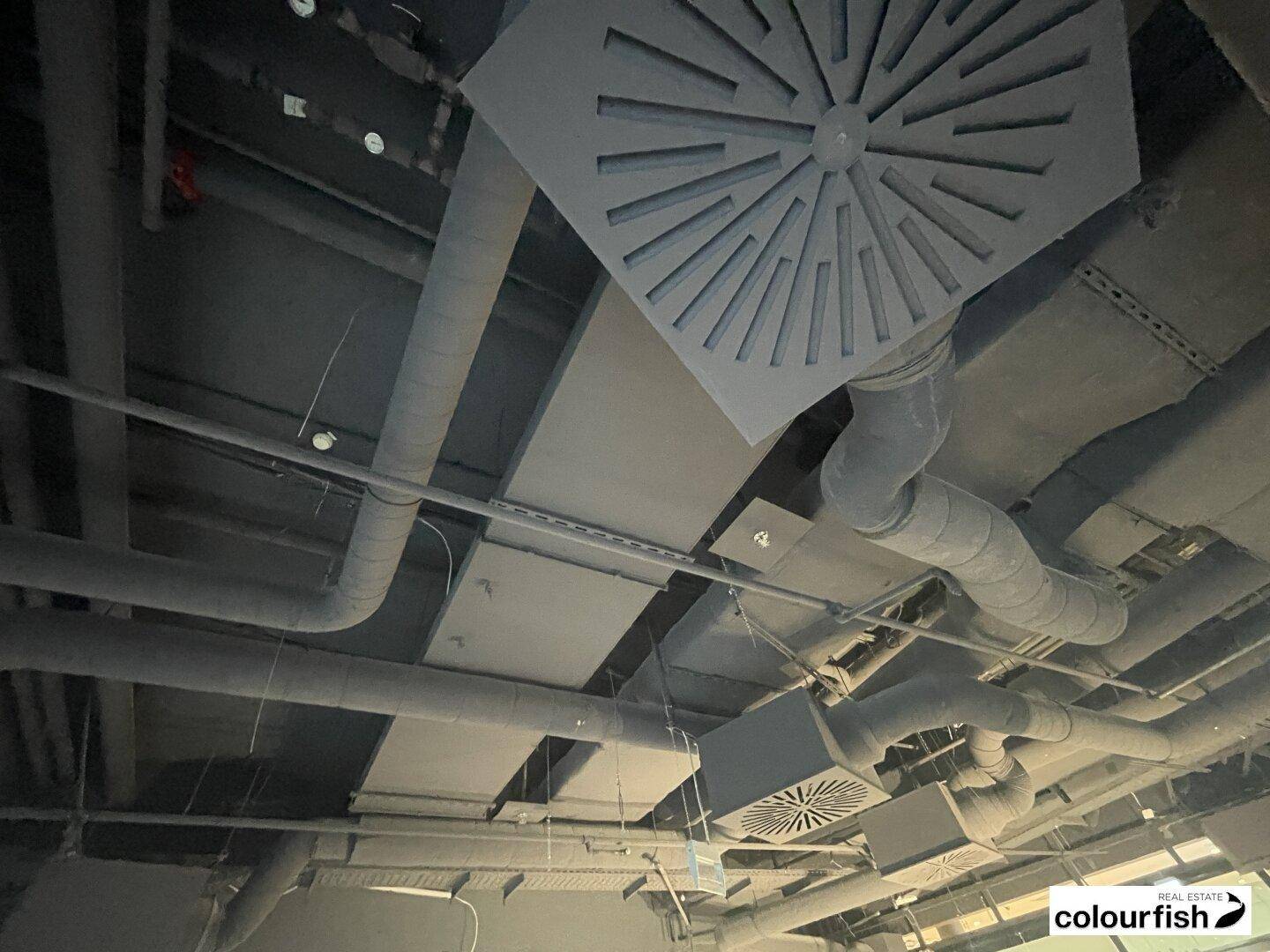 Detailaufnahme der freiliegenden Deckeninstallationen und Lüftungssysteme in einem Gewerberaum.