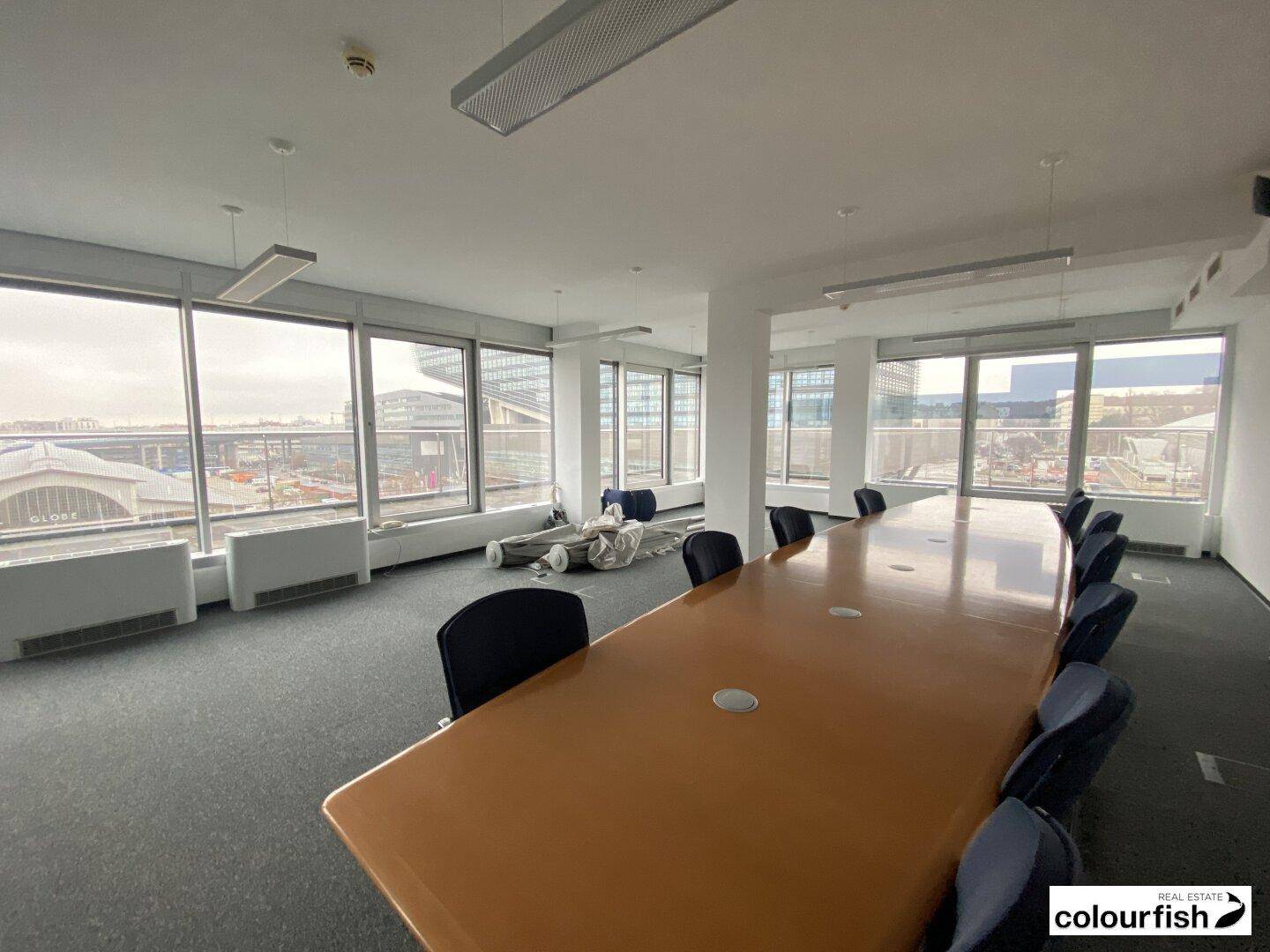 Geräumiger Konferenzraum mit großem Holztisch und Stühlen, umgeben von großen Fenstern mit Stadtblick.