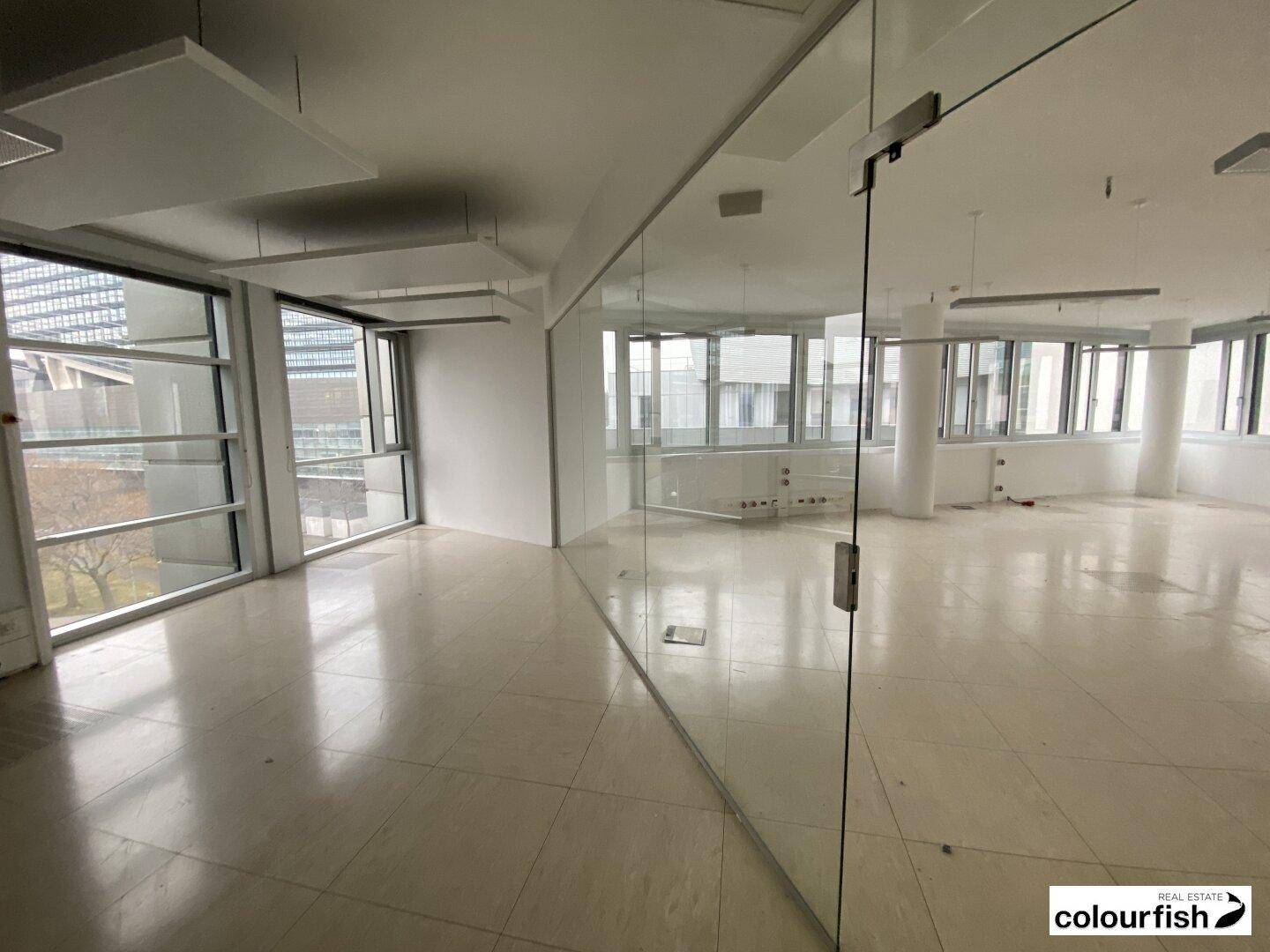 Geräumiges Büro mit Fliesenboden, Glaswänden und großen Fenstern, schafft eine offene und helle Atmosphäre.