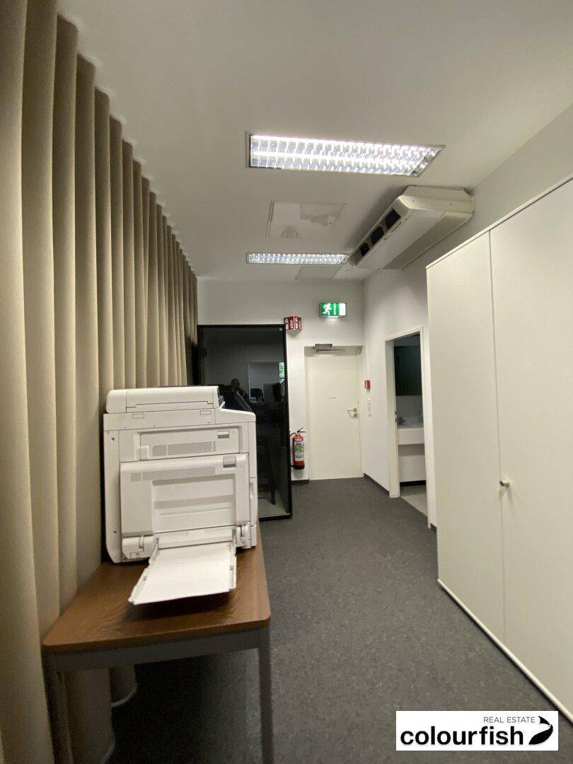 Heller Flur mit Druckerstation, Schränken und Zugang zu weiteren Räumen.