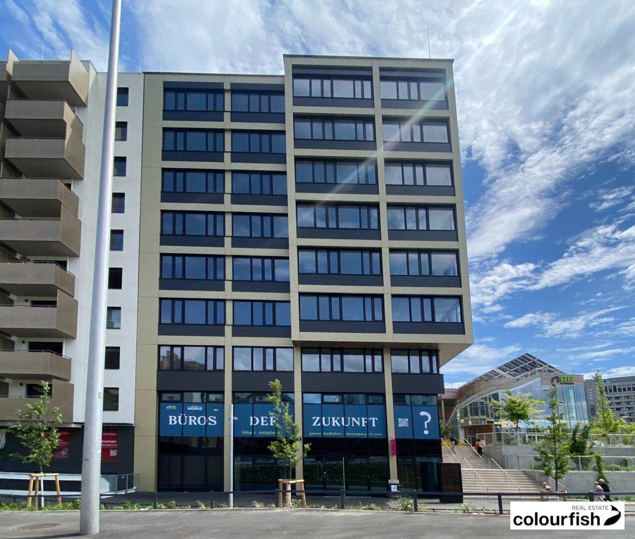 Gesamtansicht eines modernen Bürogebäudes mit vielen Fenstern und einer strukturierten Fassade unter blauem Himmel.