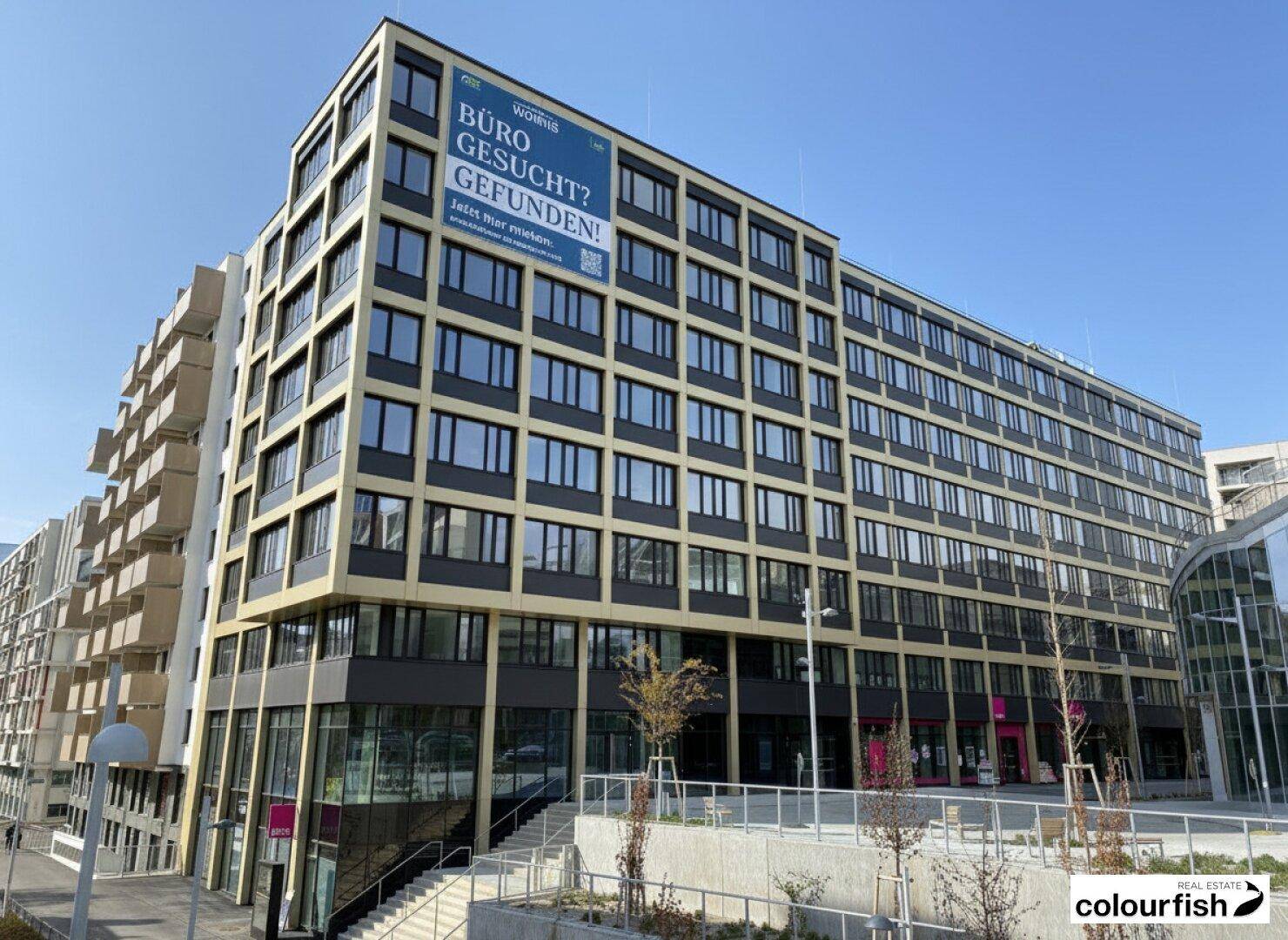 Weitläufiger Blick auf einen modernen Bürokomplex mit mehreren Etagen und großen Fensterfronten in städtischer Umgebung.