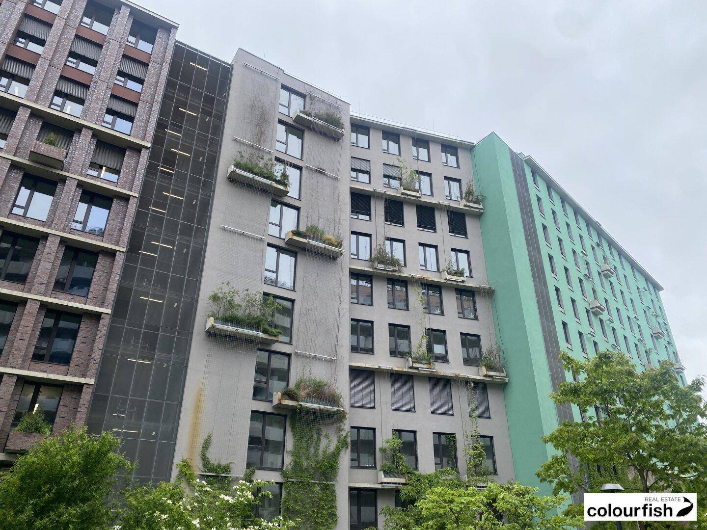 Moderne Gebäudefassaden mit vertikalen Begrünungselementen und unterschiedlichen Materialien unter bewölktem Himmel.
