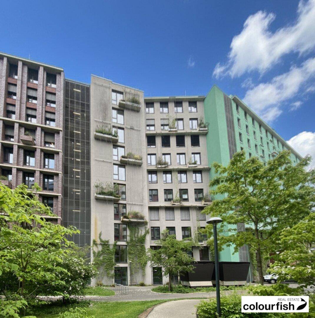 Gebäudekomplex mit modernen Fassaden und vertikaler Begrünung, umgeben von Bäumen und Grünflächen.