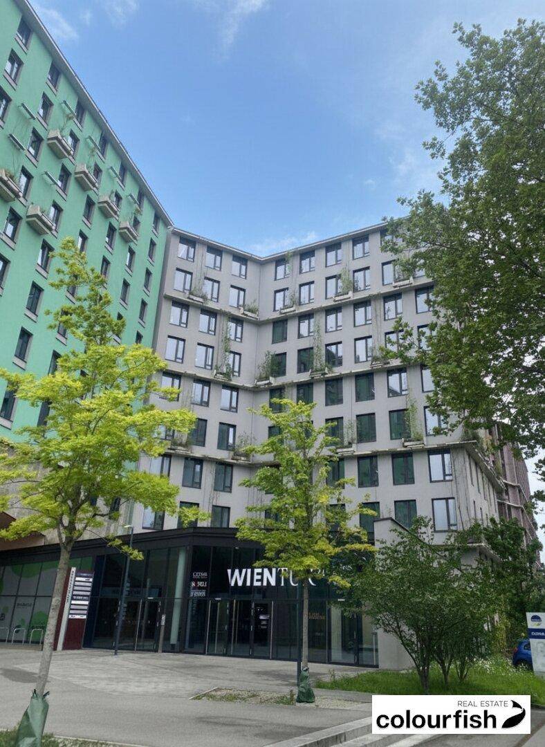 Außenansicht eines modernen Gebäudekomplexes mit grüner und grauer Fassade an einem sonnigen Tag.