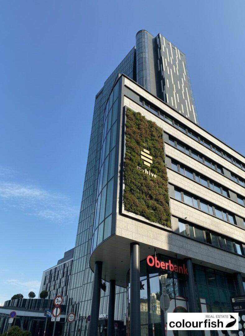 Moderne Gebäudefassade mit vertikaler Begrünung und großen Fenstern in einem städtischen Umfeld.