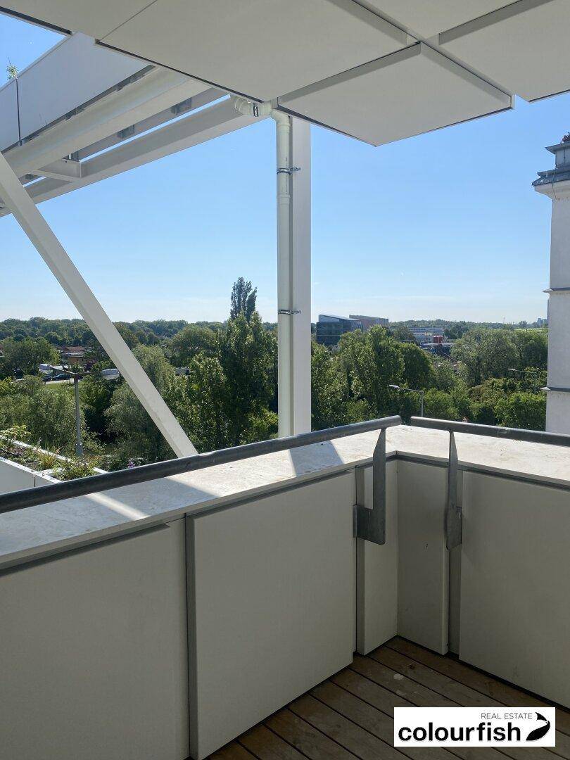 Kleiner Balkon mit Holzboden und weißem Geländer, bietet einen schönen Blick ins Grüne.
