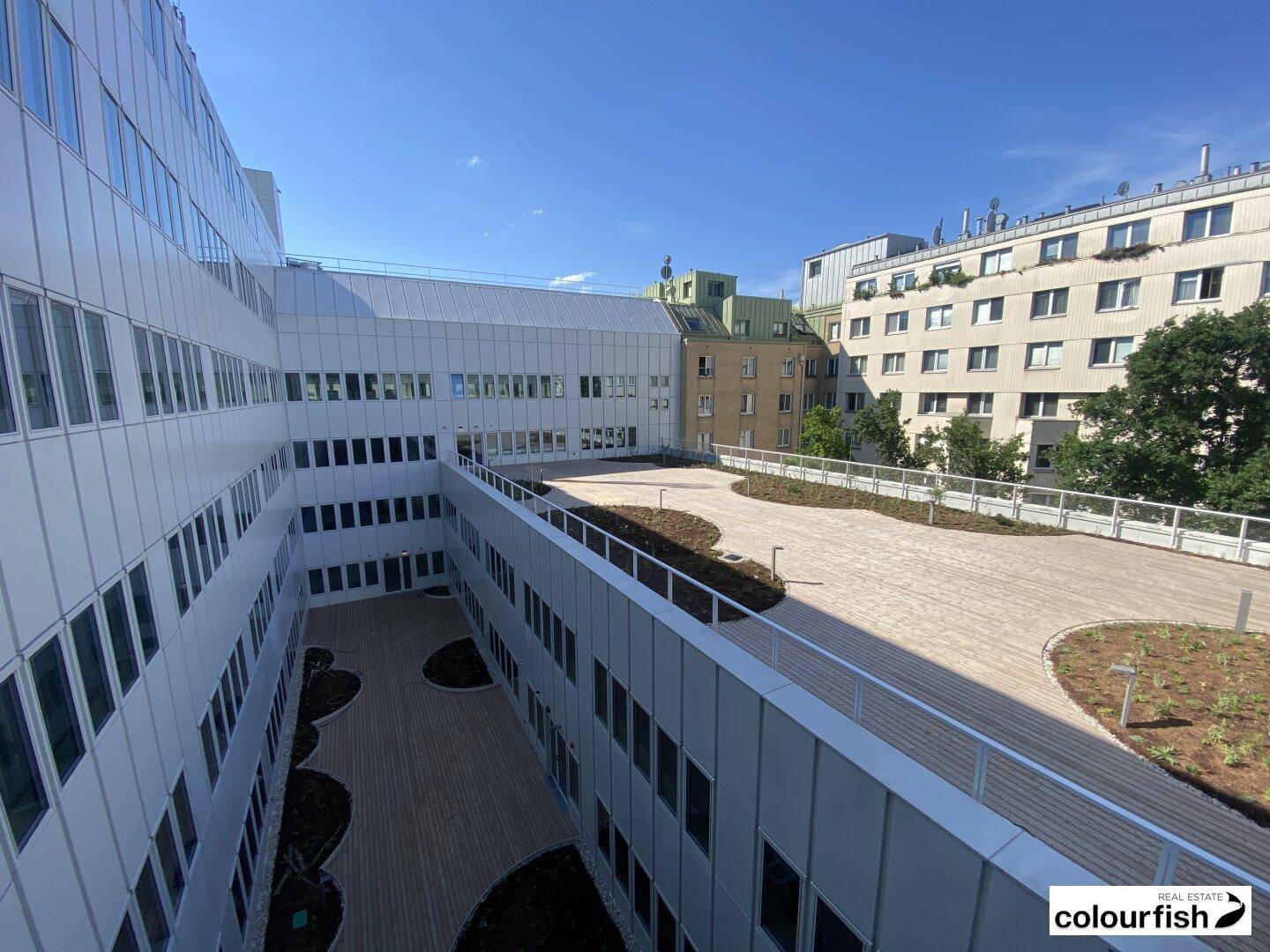 Innenhof eines modernen Gebäudekomplexes mit gepflasterten Wegen, Grünflächen und umliegenden Fassaden.
