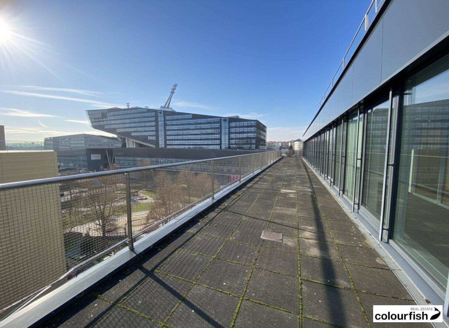 Sonnige Dachterrasse mit Blick auf markante moderne Architektur und weite Stadtlandschaft.