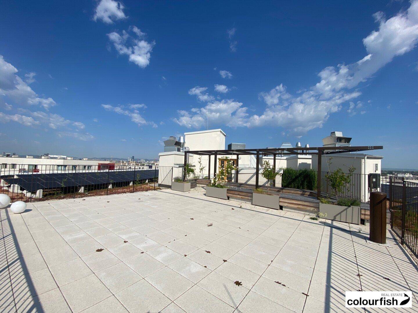 Geräumige Dachterrasse mit Steinplatten, einer Pergola und weitem Blick über die Stadt.