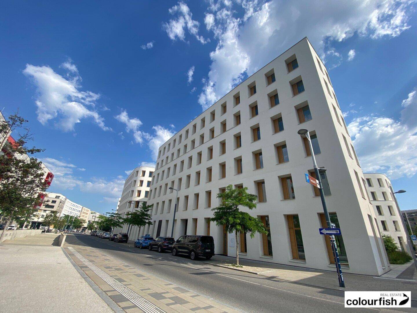 Ansicht eines modernen weißen Gebäudes mit vielen Fenstern entlang einer städtischen Straße.