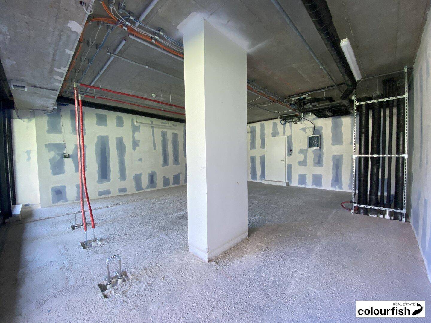 Unfertiger Innenraum mit freiliegenden Leitungen, Betonboden und vorbereiteten Wänden für den Ausbau.