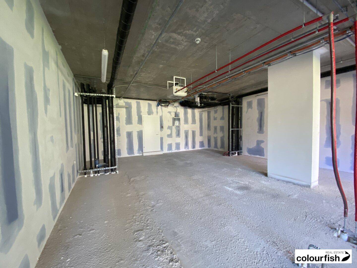 Rohbau eines Innenraums mit Betonboden, sichtbaren Installationen und vorbereiteten Wänden für den Ausbau.