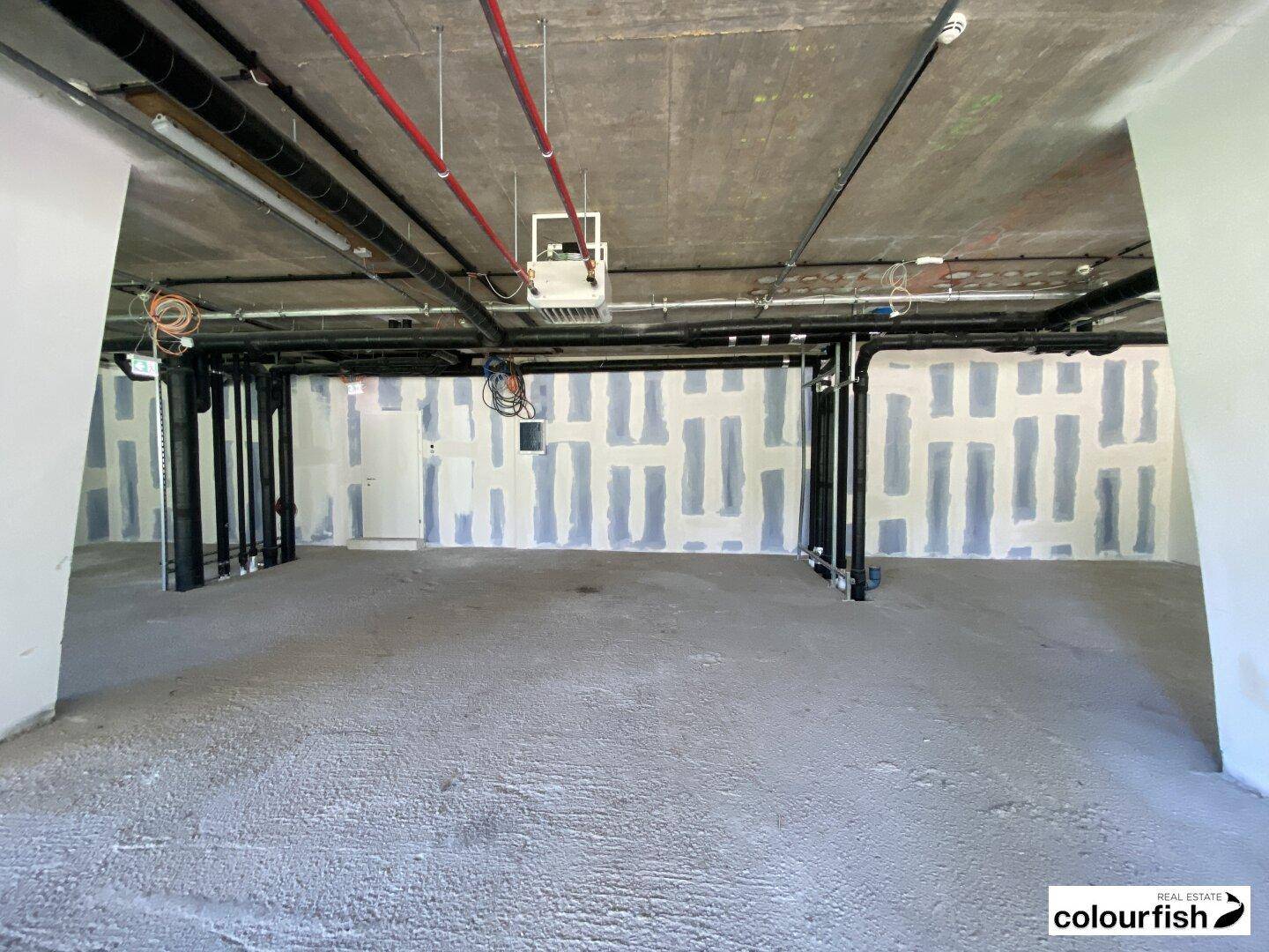 Unfertiger Gewerberaum mit teilweise verputzten Wänden, sichtbaren Rohren und Betonboden, bereit für den Ausbau.