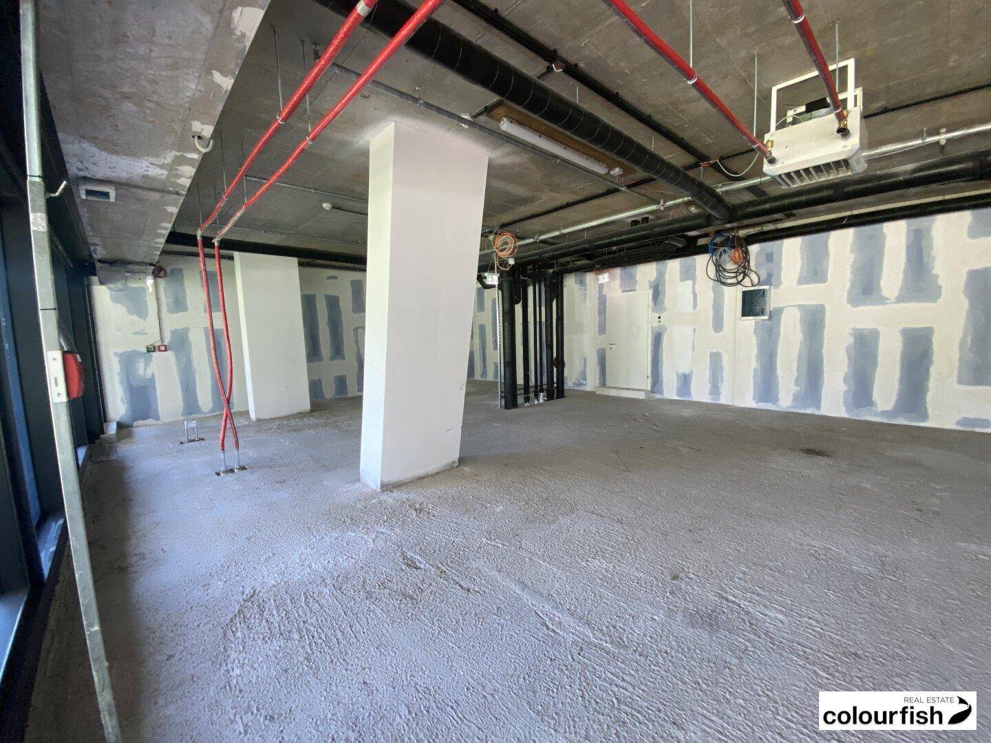 Geräumiger, unfertiger Gewerberaum mit Betonstützen, sichtbaren Installationen und vorbereiteten Wänden für den Innenausbau.