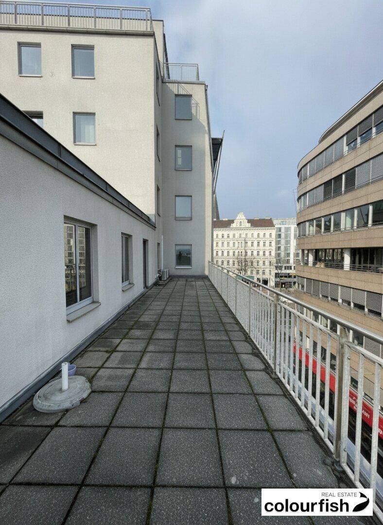 Weitläufige Außenterrasse mit Fliesenboden und Blick auf die umliegenden Stadtgebäude und moderne Fassaden.