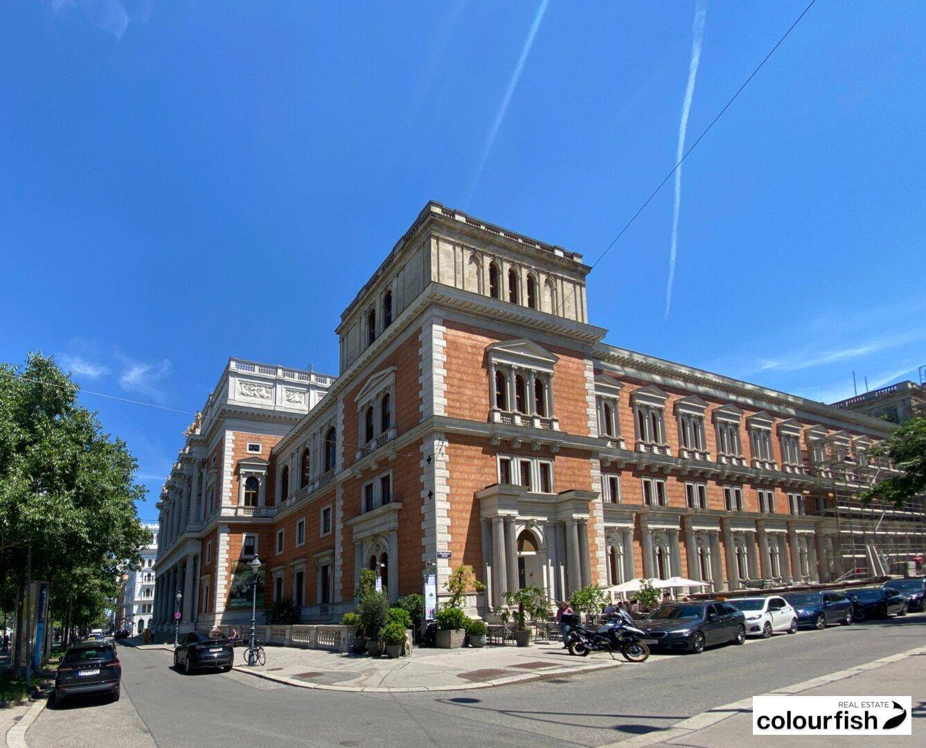 Prächtiges historisches Gebäude mit detaillierter Fassade und geparkten Autos an einer städtischen Straße.