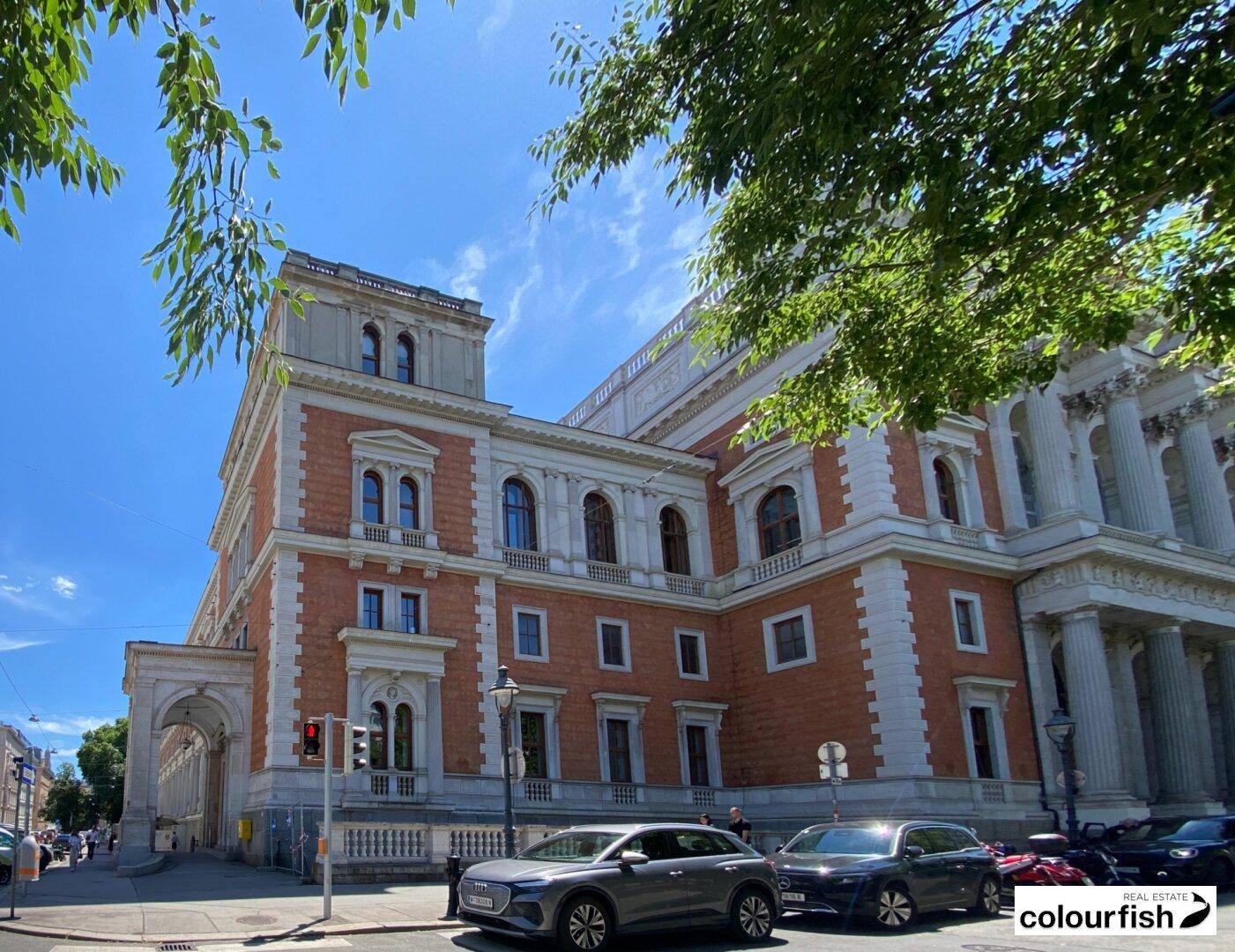 Historisches Gebäude mit klassischer Architektur, großen Fenstern und gepflegter Fassade unter blauem Himmel.