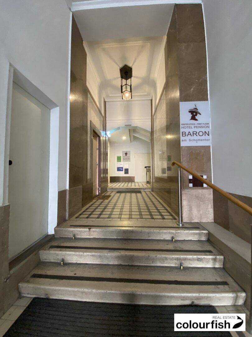 Eingangsbereich mit Marmorwänden, gemustertem Fliesenboden und einer Treppe, die zu den oberen Etagen führt.