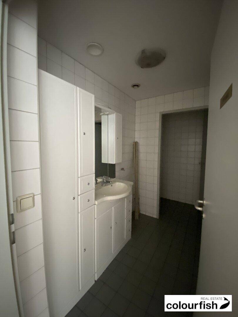 Badezimmer mit Waschbecken, Spiegel und weißen Fliesen, bietet ausreichend Stauraum.