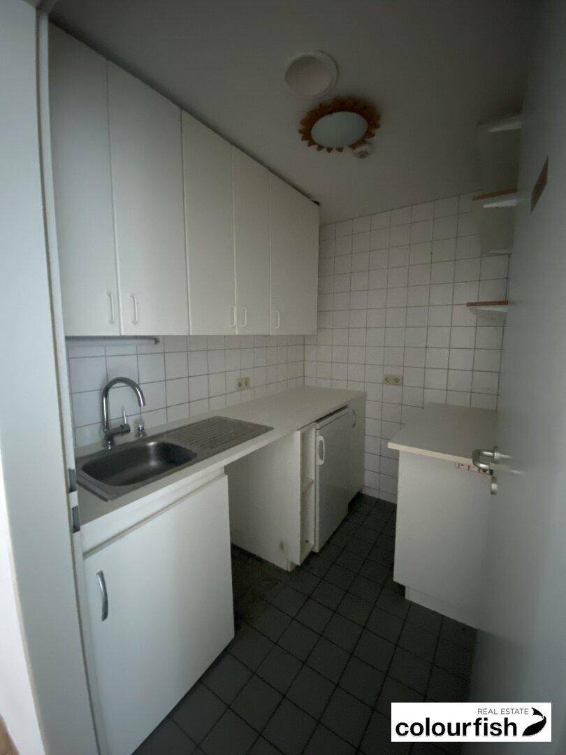 Kleine Küchenzeile mit weißen Schränken, Spüle und Fliesen an der Wand, funktional eingerichtet.