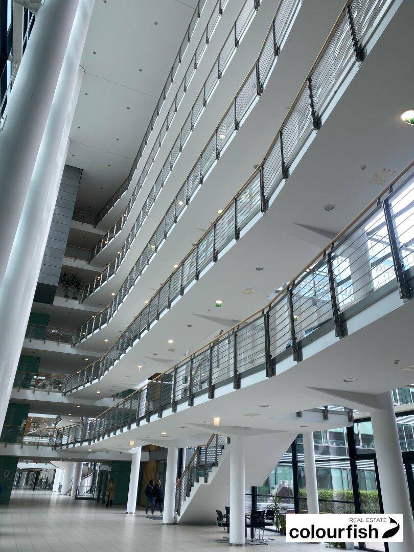 Großzügiges, helles Atrium mit mehreren Etagen und eleganten Geländern, das viel Tageslicht hereinlässt.