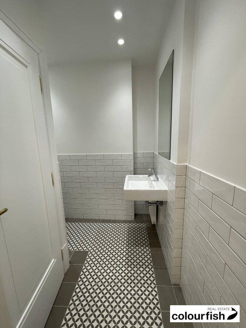 Modernes Gäste-WC mit weißen Metrofliesen, schwebendem Waschbecken und gemustertem Fliesenboden.