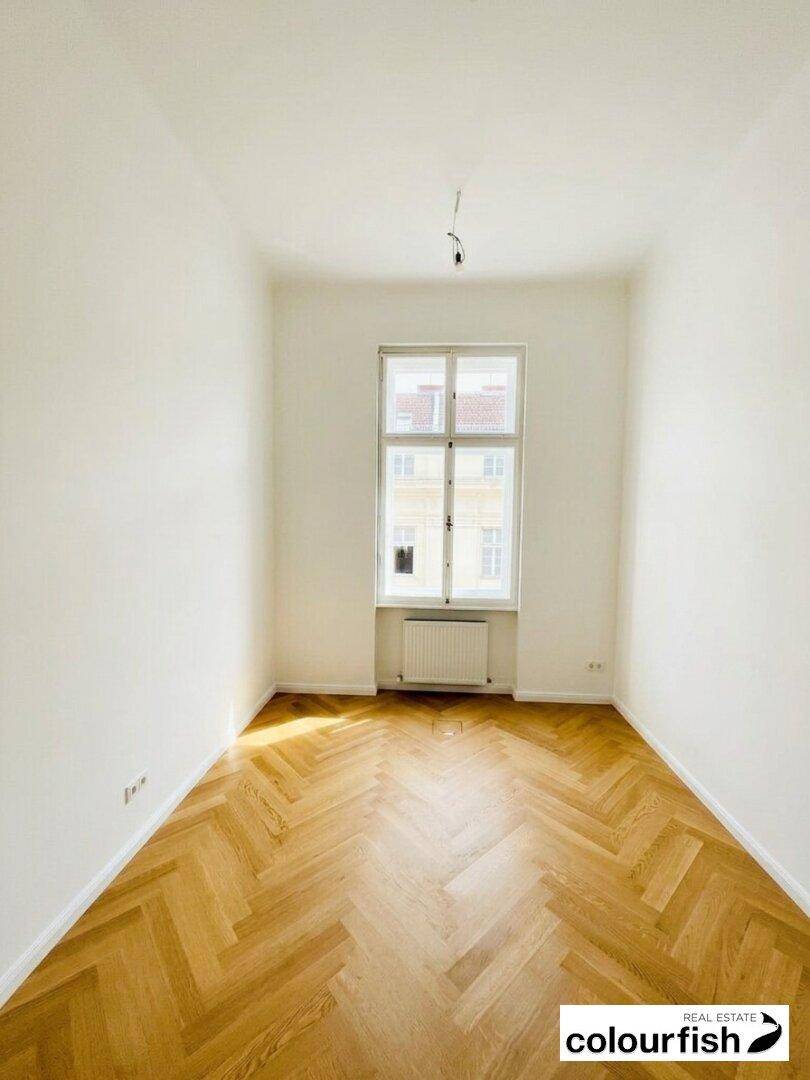 Kleiner, heller Raum mit Fischgrätparkett, weißen Wänden und einem großen Fenster, ideal für ein Büro.