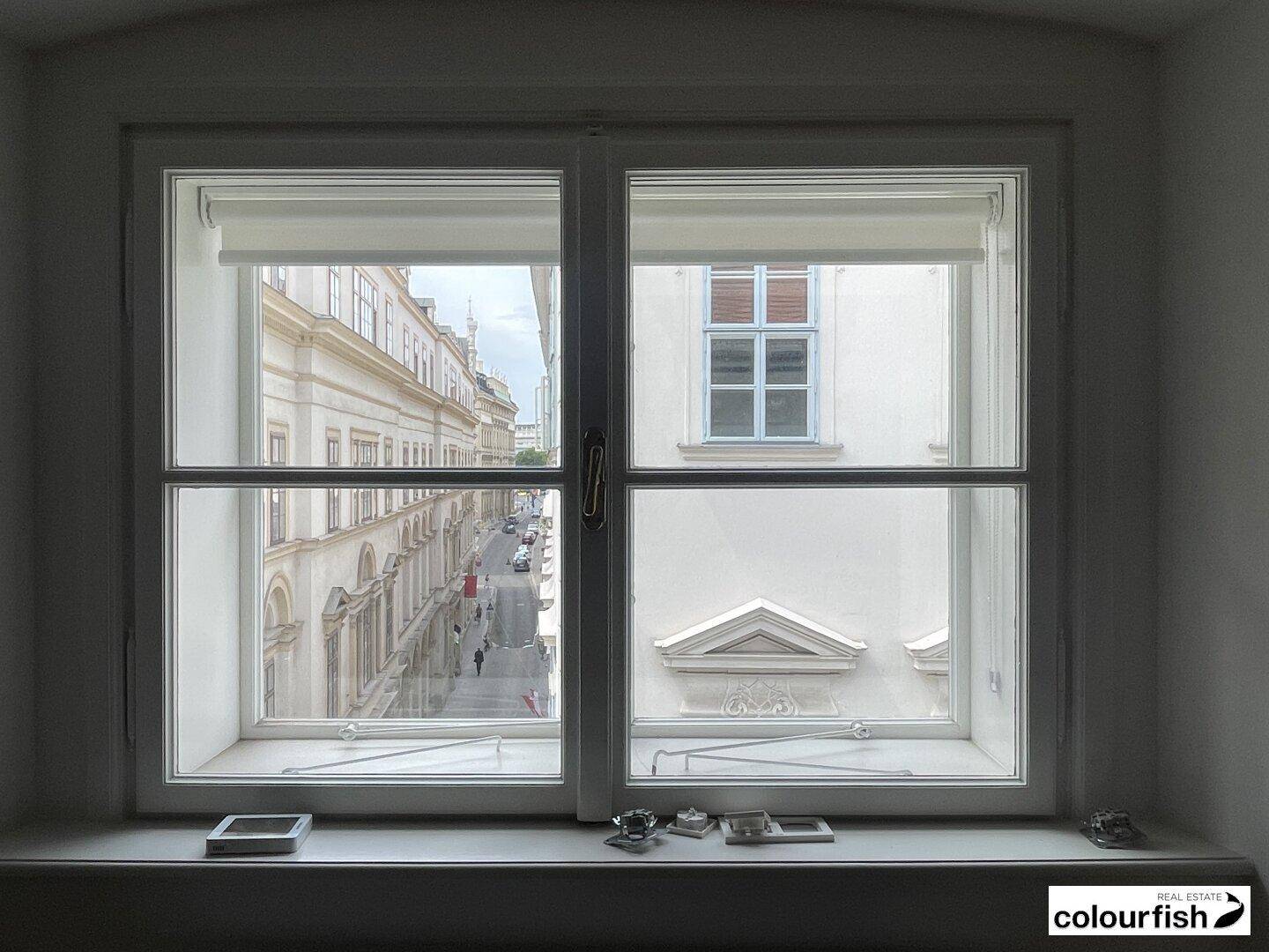 Blick aus einem Fenster auf eine belebte Straße und die gegenüberliegenden historischen Gebäude.