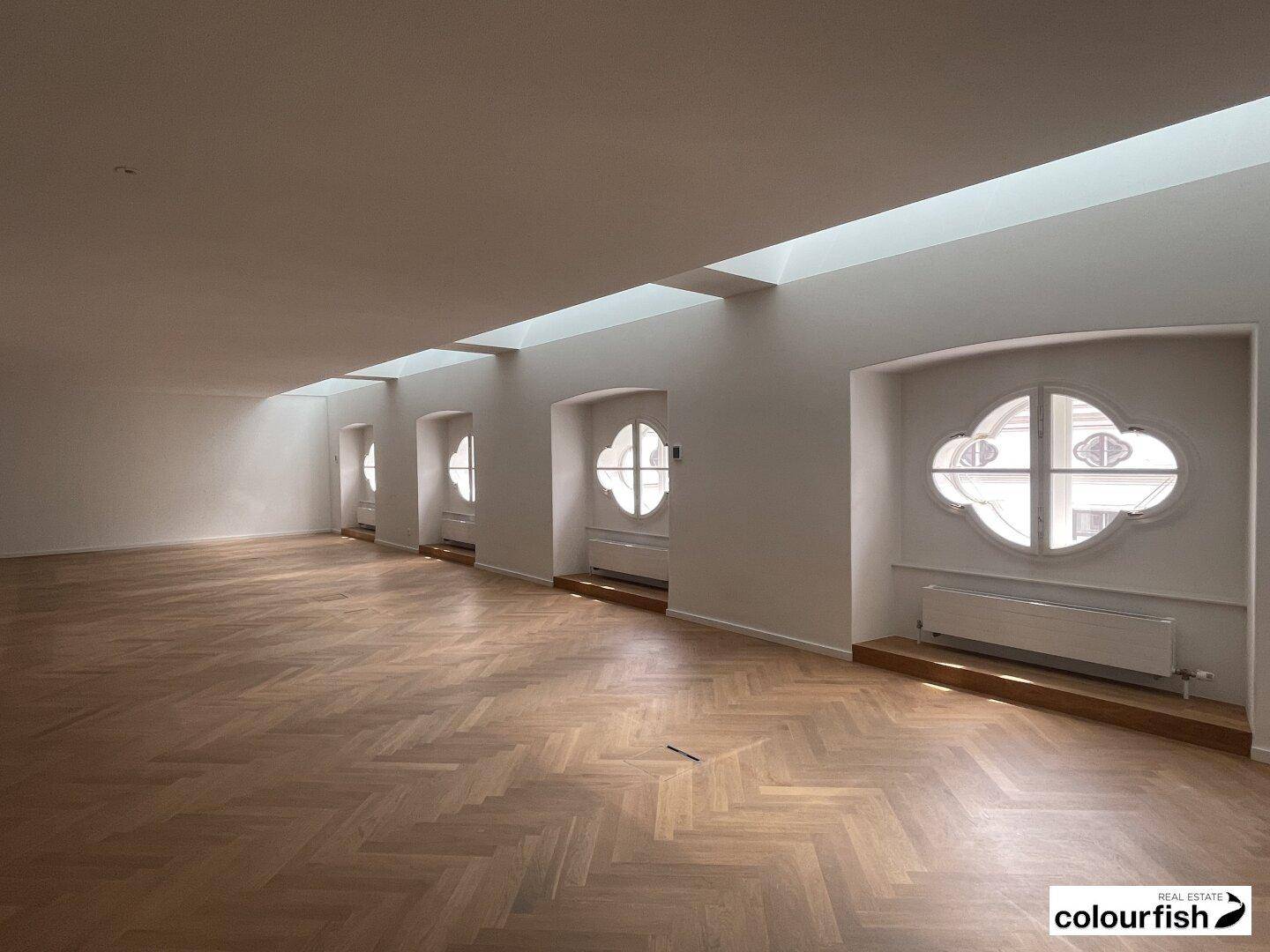 Langer, heller Raum mit einer Reihe von kleeblattförmigen Fenstern und elegantem Fischgrätparkett.