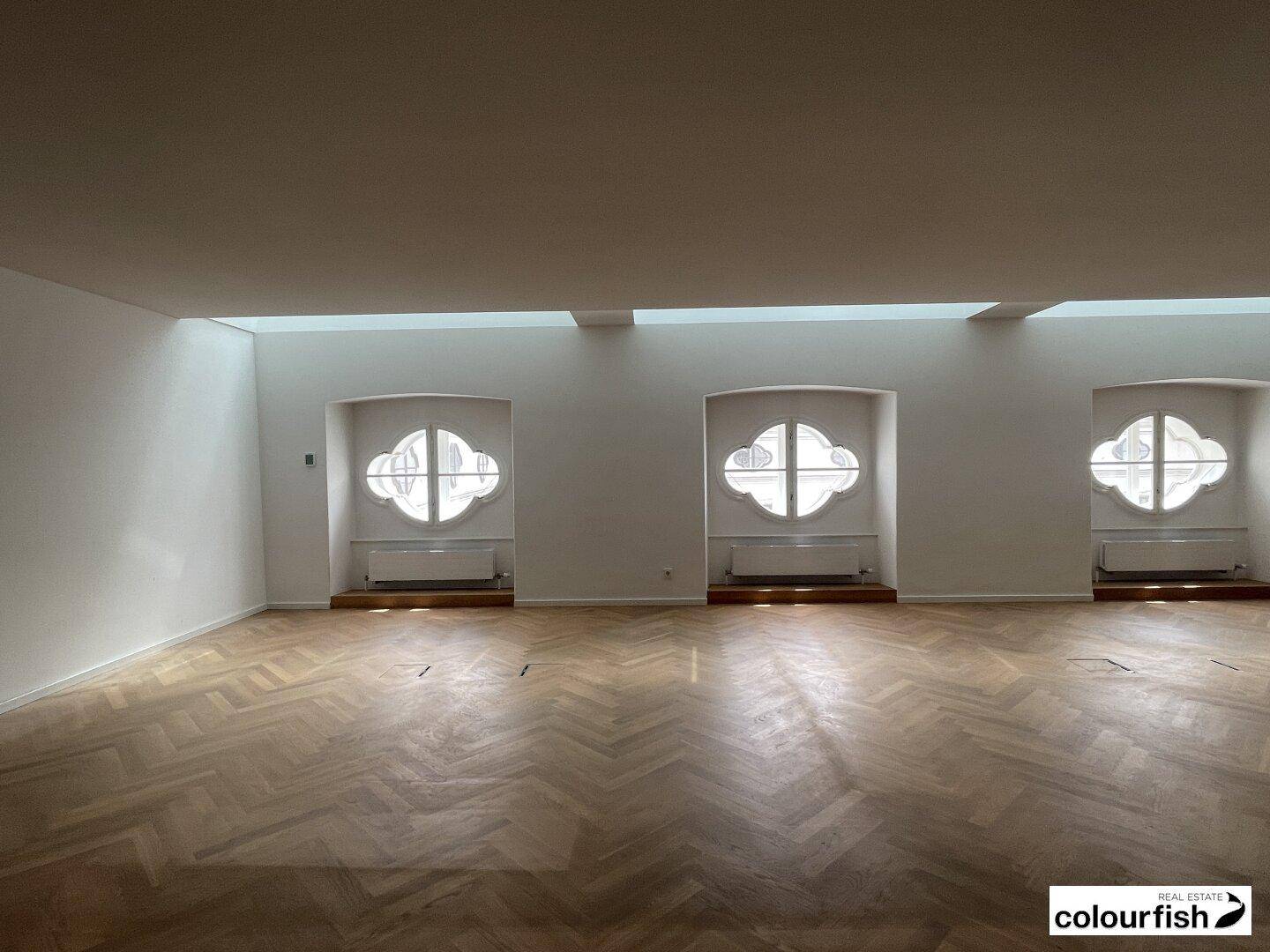 Weitläufiger Raum mit drei markanten kleeblattförmigen Fenstern und viel natürlichem Lichteinfall.