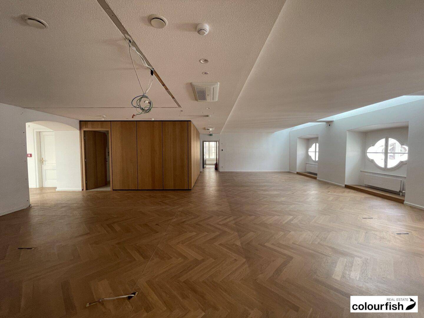 Weitläufiger Raum mit Fischgrätparkett und einer eleganten Holzwandverkleidung oder Einbauschränken.