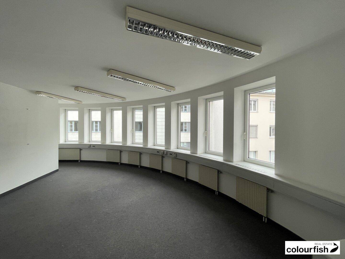 Geschwungener Büroraum mit einer Reihe von Fenstern, die viel natürliches Licht hereinlassen.